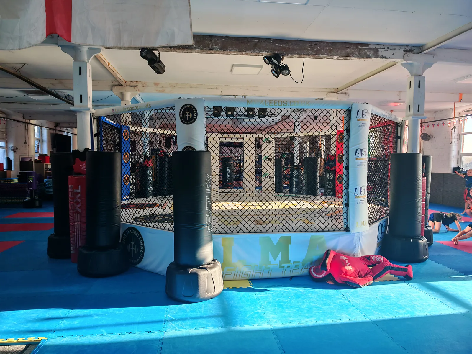 The main LMA training floor with blue mats, red training squares and an MMA cage