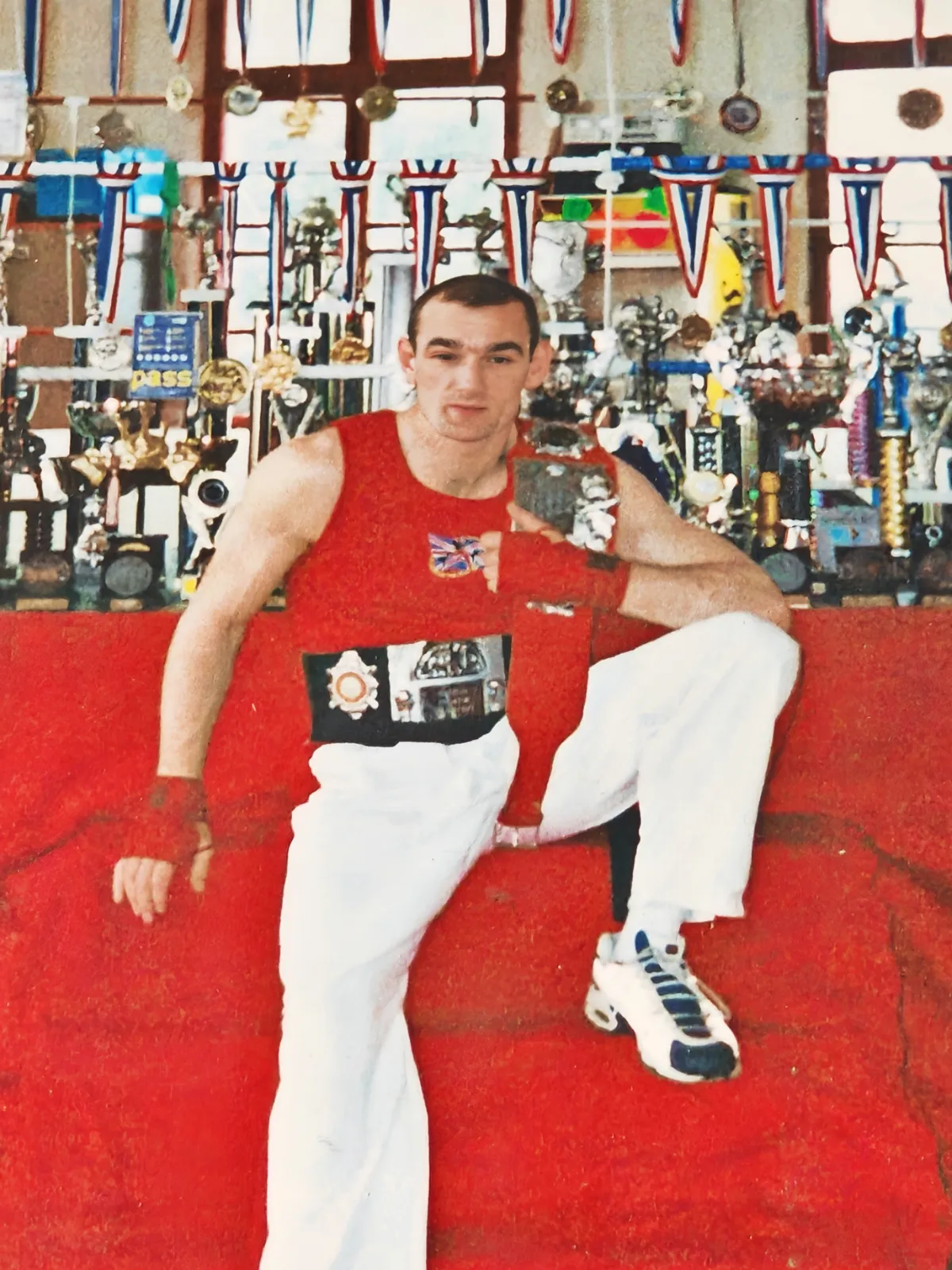 Paul Lynch seated among trophies and medals from his kickboxing career in the 1990s